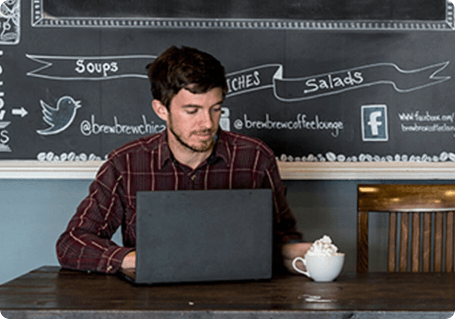 A man at a cafe with his computer and Reddiwip topped coffee beverage.